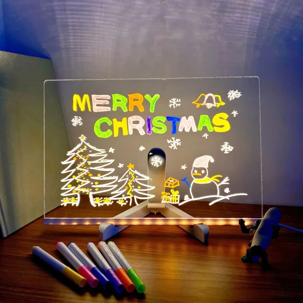 Christmas-themed LED sign with 'Merry Christmas' text and festive illustrations on a stand, with markers on a wooden surface.