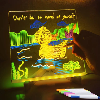 Light-up drawing board with colorful drawing and text 'Don't be so hard on yourself' in a dark setting.